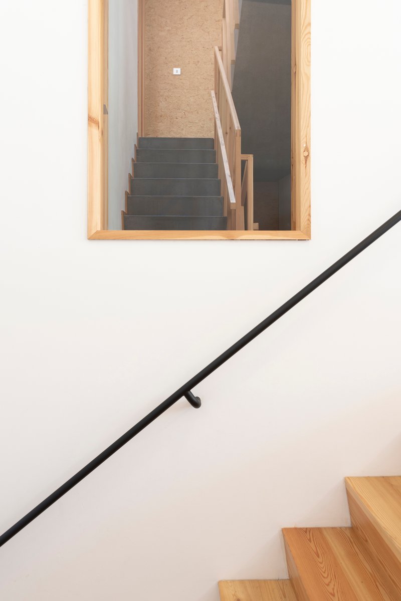 Stairwell with black metal handrail against white wall and timber-framed opening revealing upper level