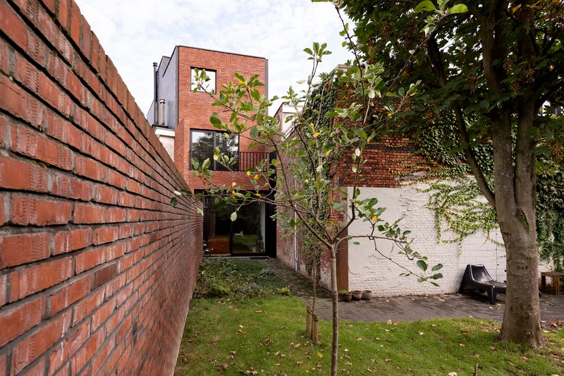 Rear garden courtyard with red brick walls, young trees and a painted white adjoining structure