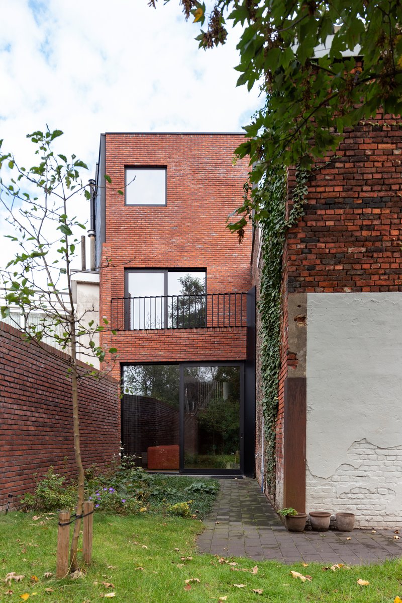 Narrow brick facade with stacked windows and a glass door opening to a planted garden