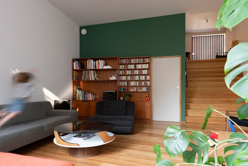 Living room with a dark green accent wall, timber bookshelves and a person in motion