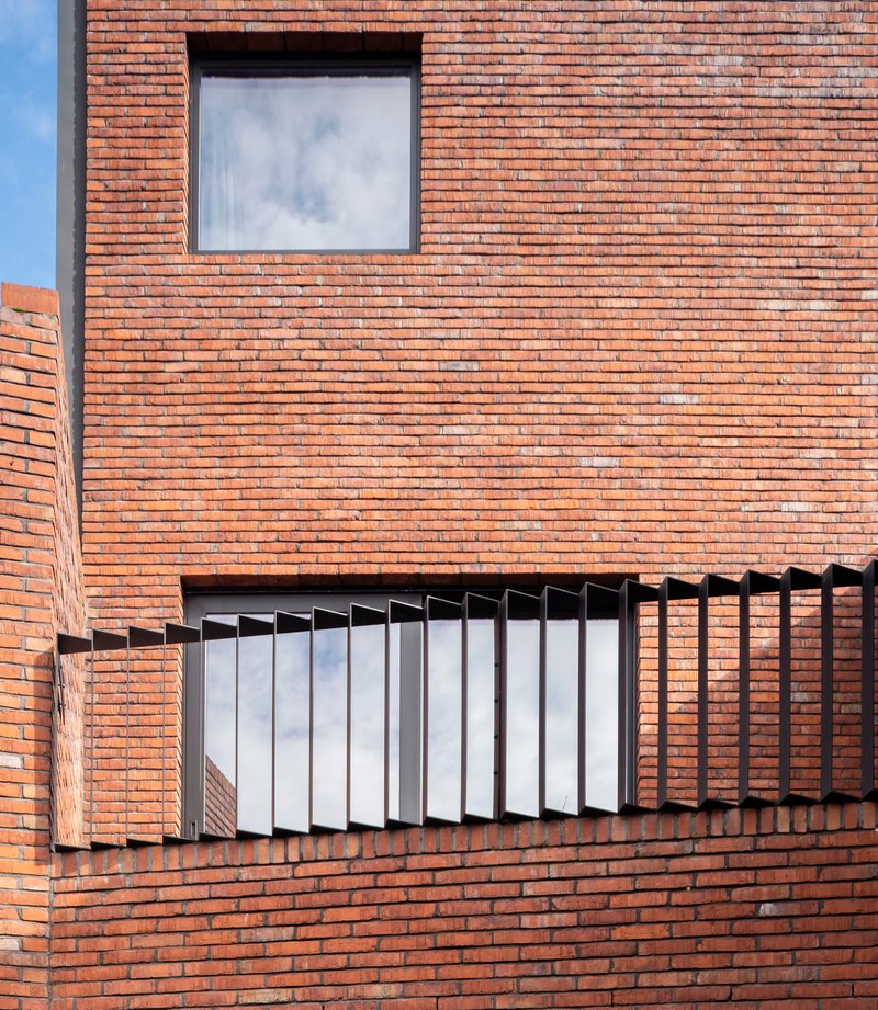 Orange brick facade with folding white metal louvers framing a recessed balcony opening