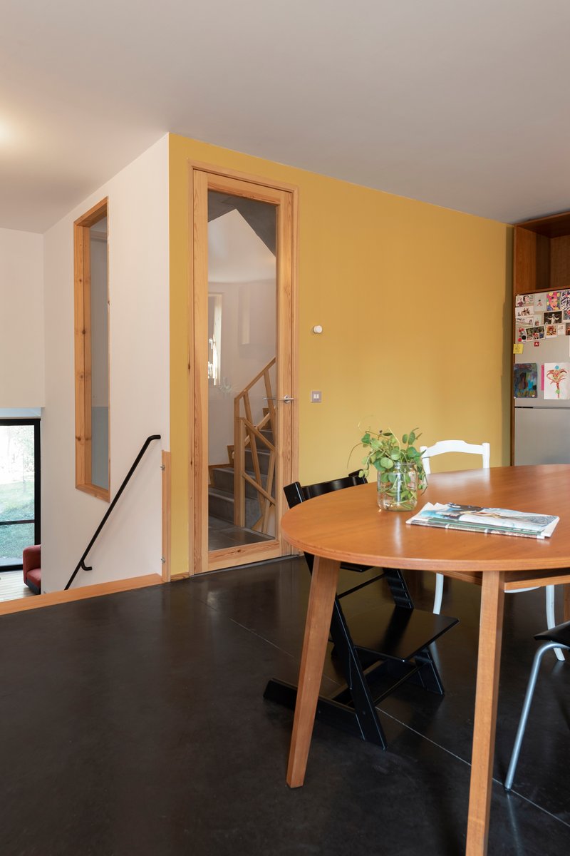 Dining area with timber doorway framing view to staircase and yellow accent wall