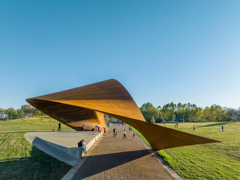 Elevated concrete plaza beneath the lifted steel canopy with families walking in late afternoon light