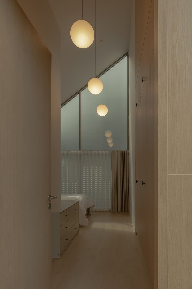 Corridor view through angled glass partition with suspended globe pendants and translucent curtain