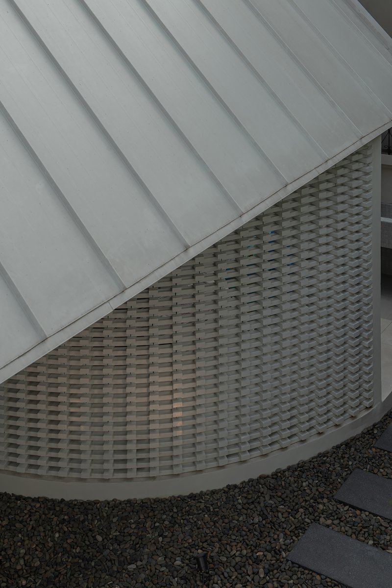 Detail of curved woven brick facade beneath metal standing seam roof and gravel courtyard