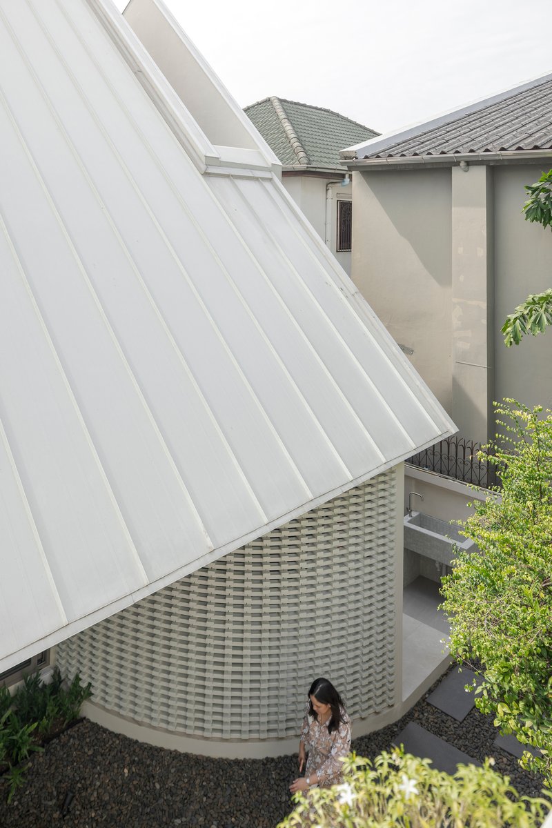 White ribbed metal roof plane rising above a woven brick wall with a woman walking below