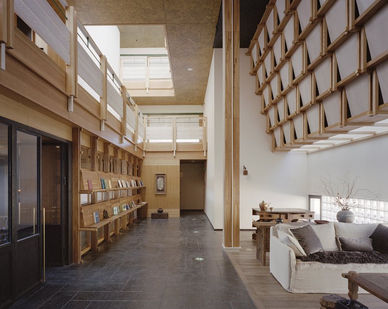 Double-height lobby with timber shelving, exposed wooden columns, and skylights above a seating area