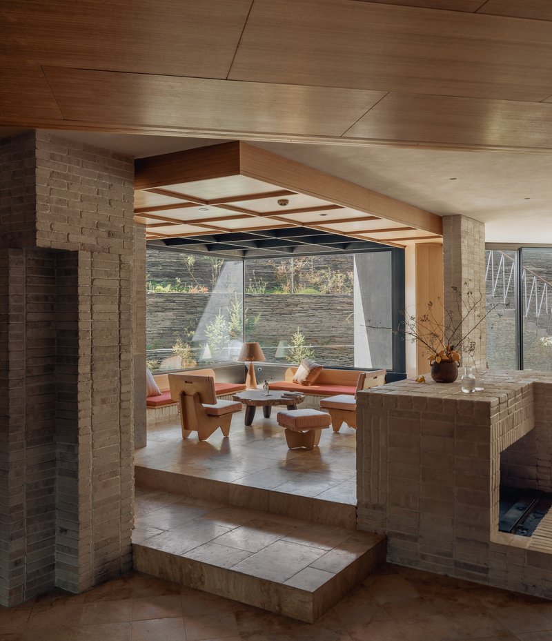 Sunken living area framed by brick columns and timber ceiling beams with glazed walls beyond