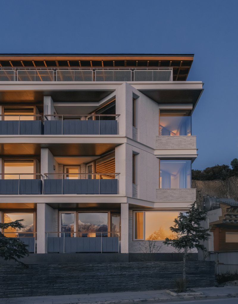 Three-story facade detail showing deep balconies and corner glazing at twilight