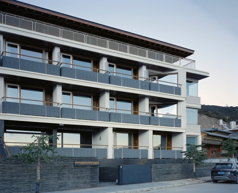 Street facade showing three-story elevation with continuous balconies and dark stone base wall at dusk