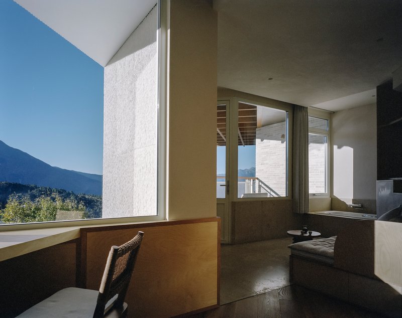 Interior corner desk overlooking mountain landscape through floor-to-ceiling glass under clear blue sky