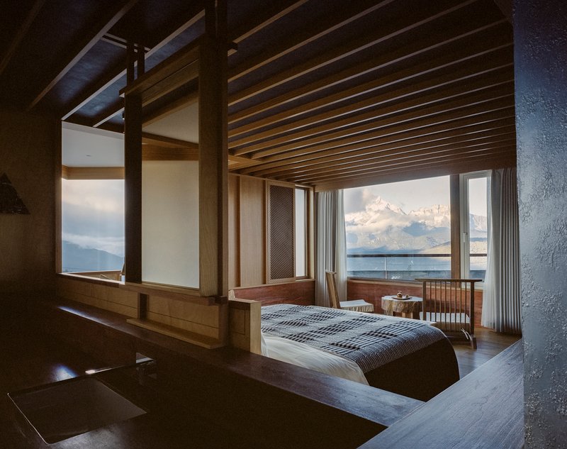 Bedroom with exposed timber beams and full-height windows facing distant clouds and lake