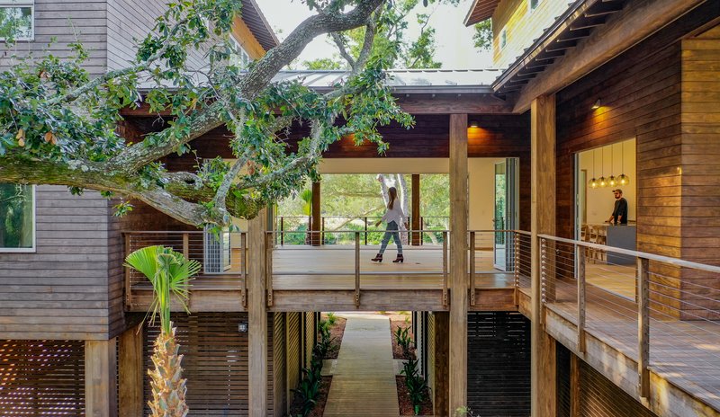 Covered walkway connecting timber volumes with a figure crossing the elevated deck between buildings