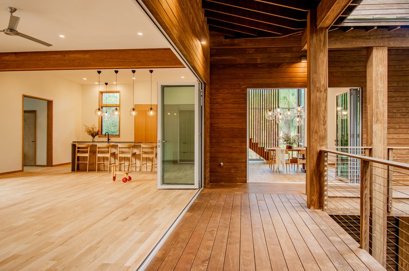 Open-plan living space with exposed wood ceiling beams and horizontal plank walls opening to deck