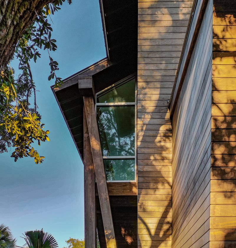 Angled timber column supporting the deep eave with dappled afternoon shadows on the siding
