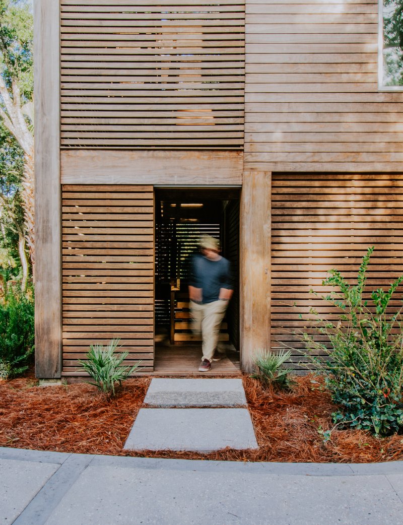 Entry threshold with horizontal slatted timber screen and figure in motion crossing planted beds