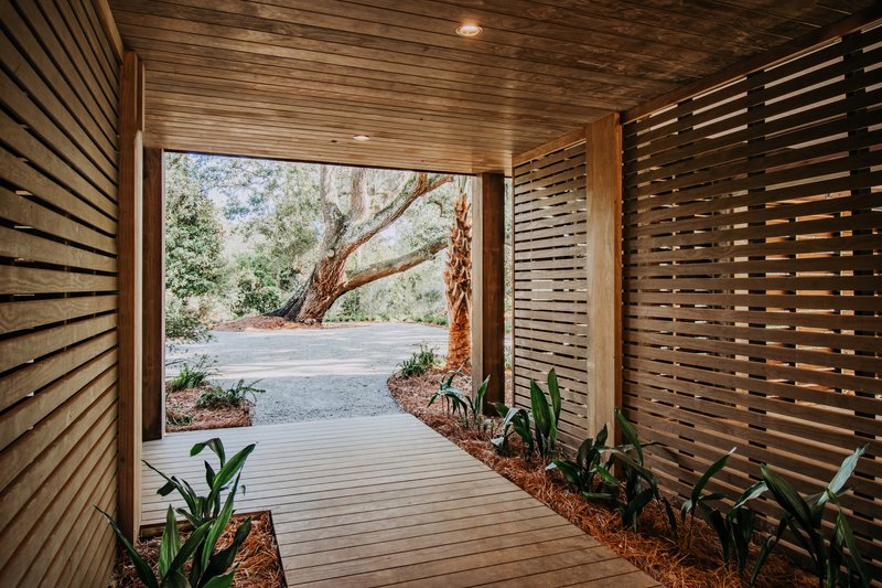 Covered timber walkway with slatted screen walls framing a view of an oak tree beyond