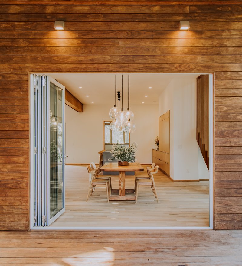 View through folding glass doors into dining room with timber walls and pendant lighting