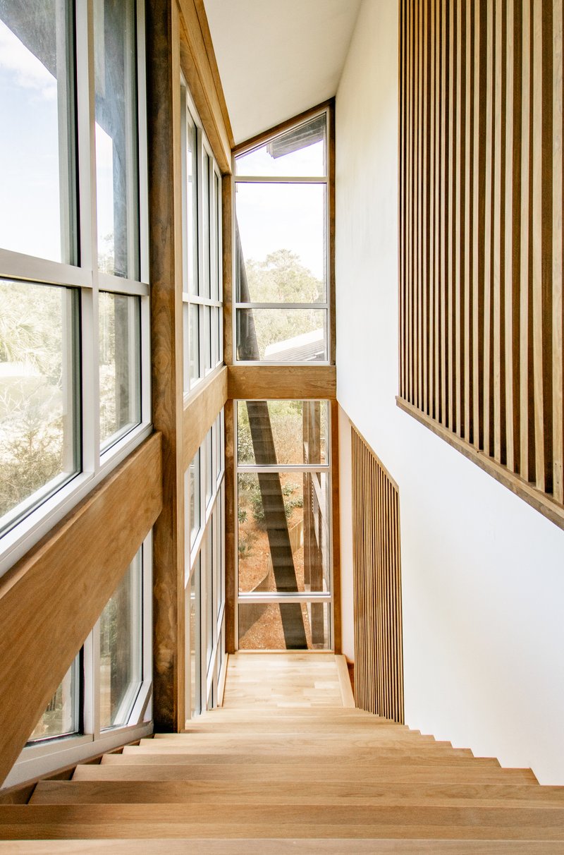 Timber staircase descending alongside floor-to-ceiling windows with vertical wood slat screens on white walls