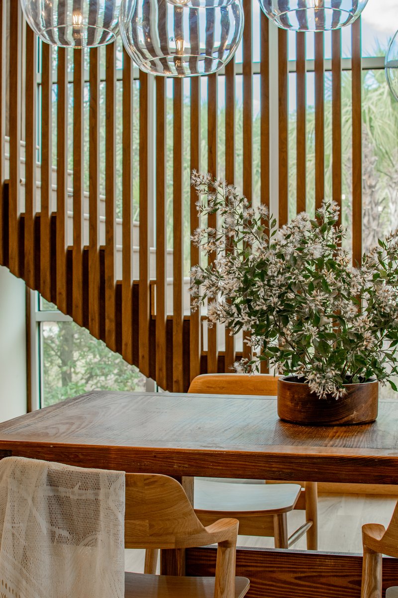 Dining table with clear glass pendant lights and flowering branches against vertical timber batten wall