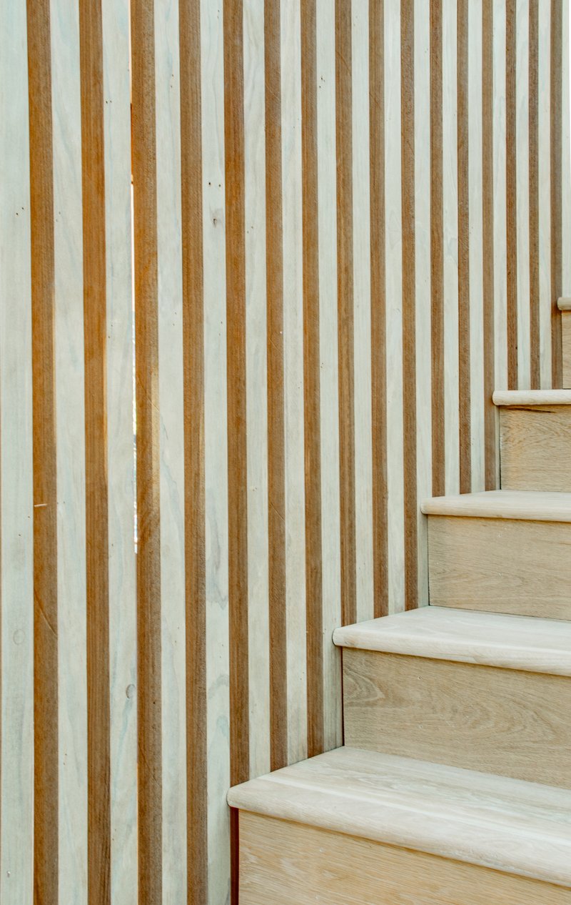 Close-up of pale wood stair treads meeting a vertical slatted timber and plaster wall