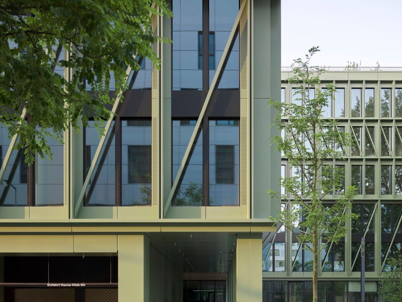 Facade detail showing diagonal yellow bracing columns and young street trees against a white sky