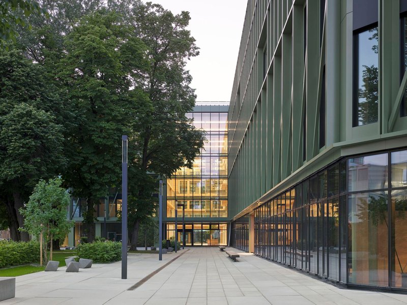 Paved plaza between two volumes with vertical green cladding and mature trees at dusk