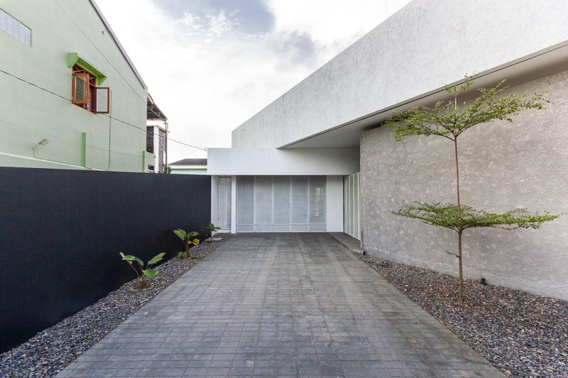 Paved entry drive with a young tree in gravel planting bed beside textured concrete walls