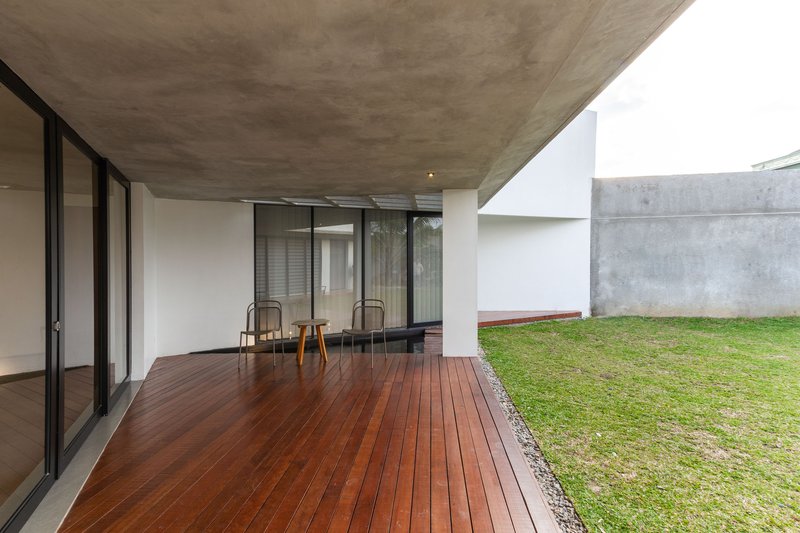 Covered terrace with timber decking and two chairs overlooking a grassed courtyard with concrete walls