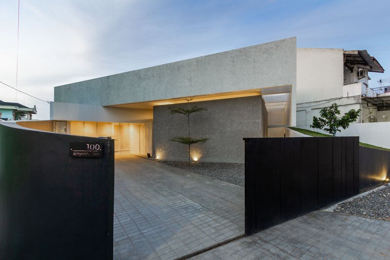 Street view of the concrete entrance with illuminated carport and black metal sliding gate at dusk