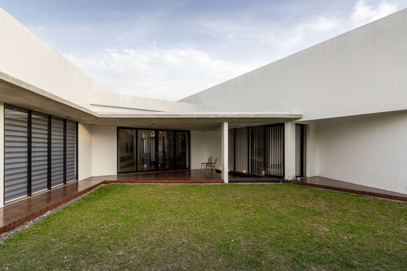 Private courtyard with grass lawn bordered by timber deck and white rendered walls under cloudy sky