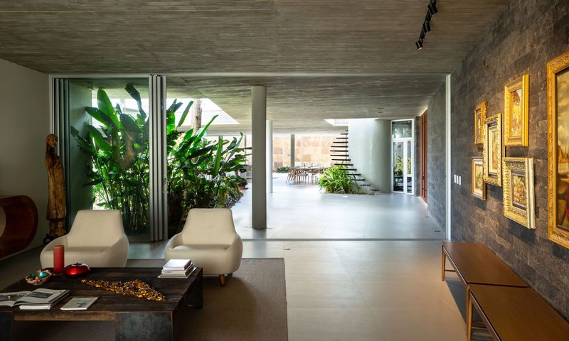 Living room view through to interior courtyard planted with tall banana palms under exposed concrete ceiling
