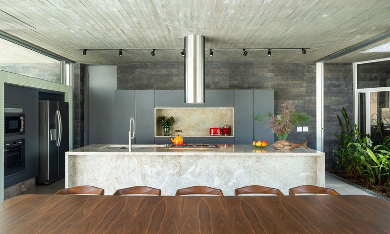Kitchen island with veined marble counter and suspended cylindrical steel hood beneath board-formed concrete ceiling