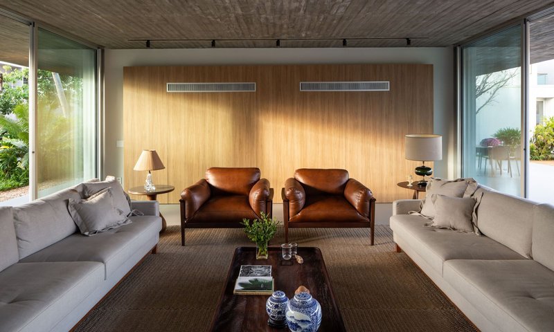 Sitting room with timber-paneled wall, glazed corners opening to garden, and afternoon sunlight filtering in