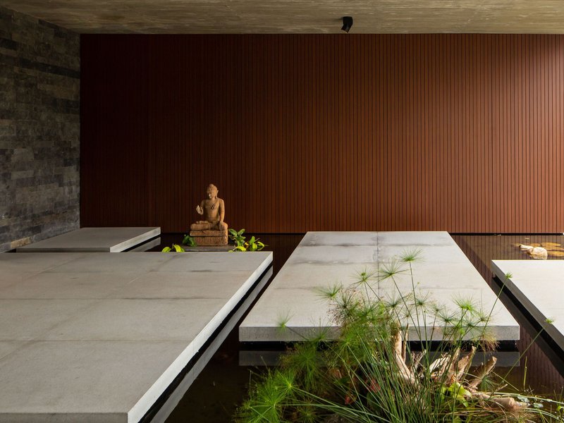 Interior courtyard with concrete platform over reflecting pool, vertical wood wall and stone Buddha sculpture