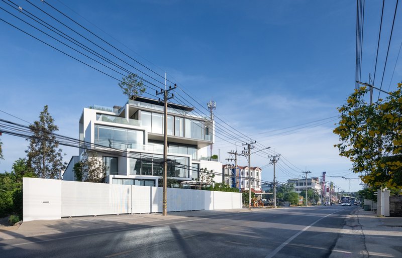 Street view of white stacked volumes with full-height glazing beneath clear blue sky and overhead power lines