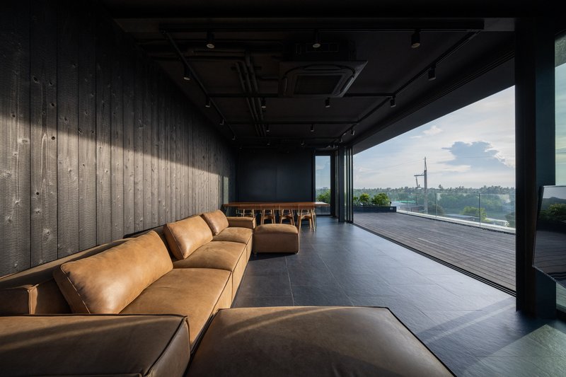 Interior lounge with leather seating and charred timber walls opening to a deck at dusk