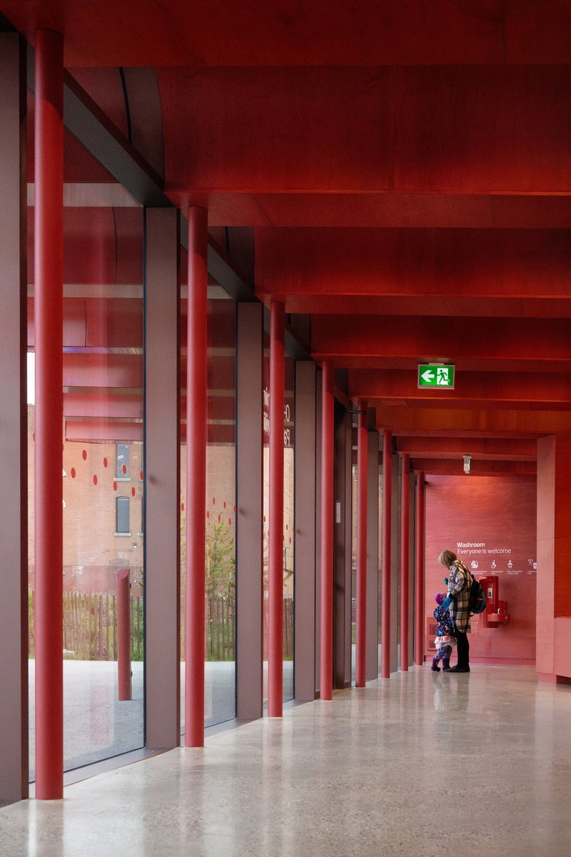 Interior corridor with red steel columns and red-painted ceiling beams with a figure walking
