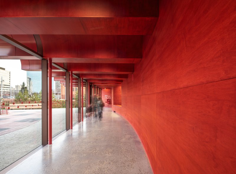 Red-washed corridor with terrazzo flooring and glazed wall overlooking planted courtyard in daylight