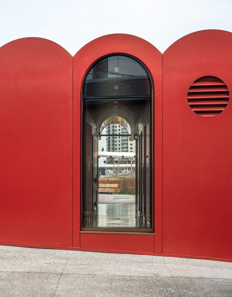 Arched doorway in red facade with circular vent opening and glazed entrance looking through to street