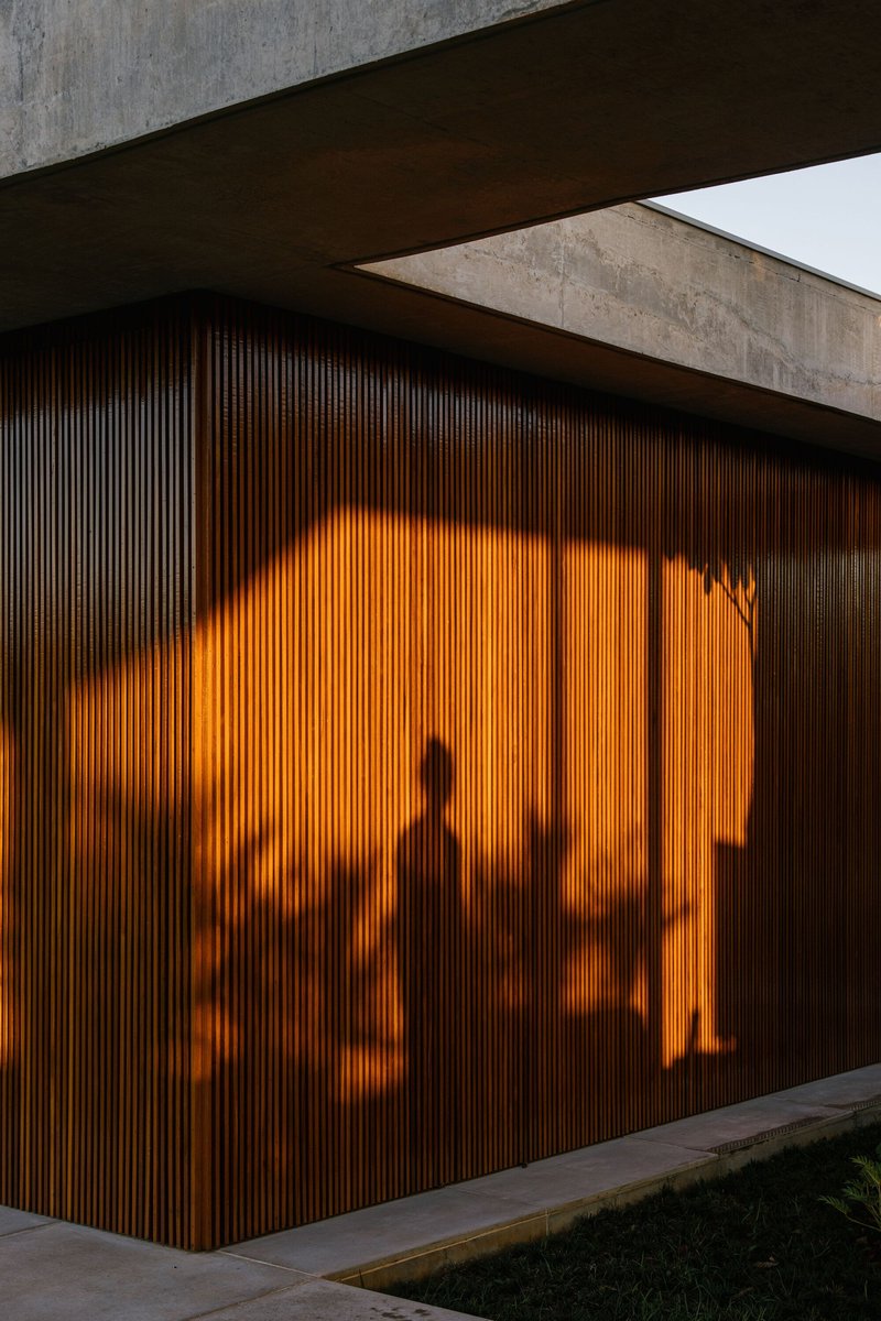 Vertical timber screen wall with silhouettes of interior figures illuminated by warm light at dusk