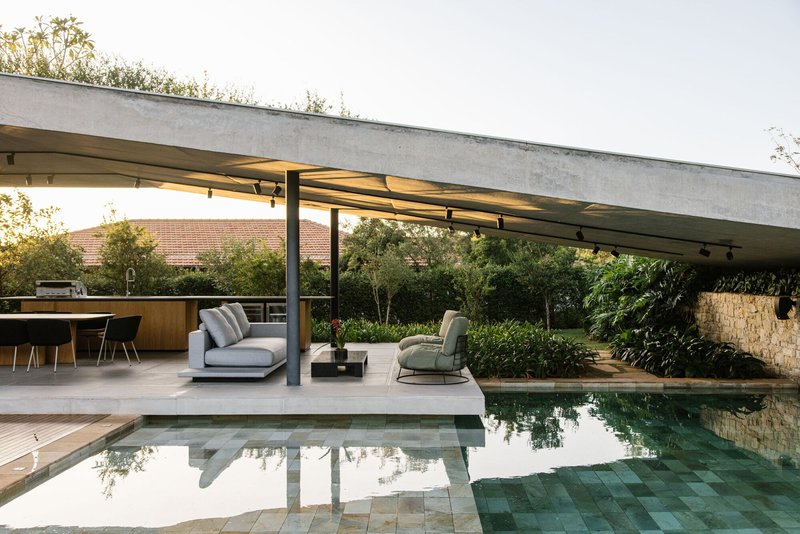 Pool deck and covered pavilion reflected in still water with planted roof garden beyond