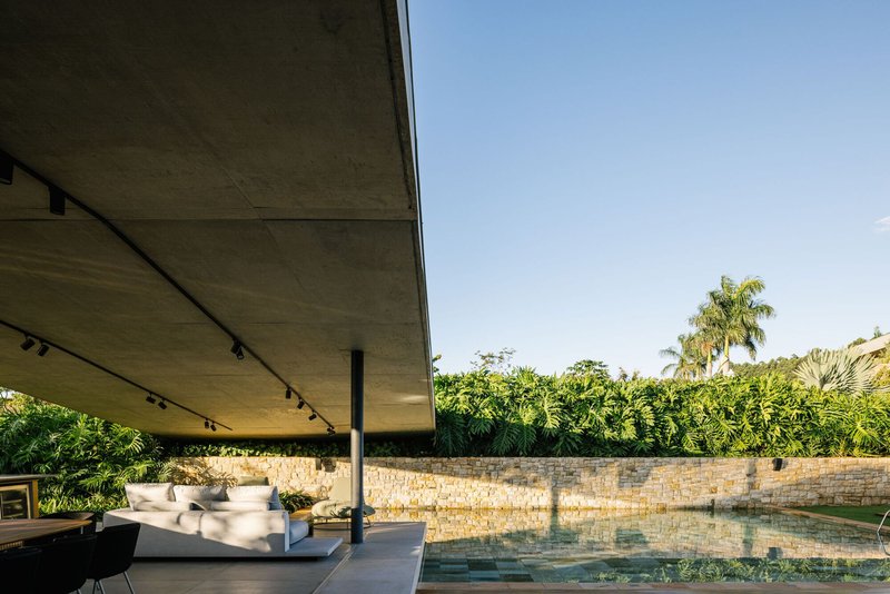 Covered pool terrace with exposed concrete soffit and limestone retaining wall beyond the water