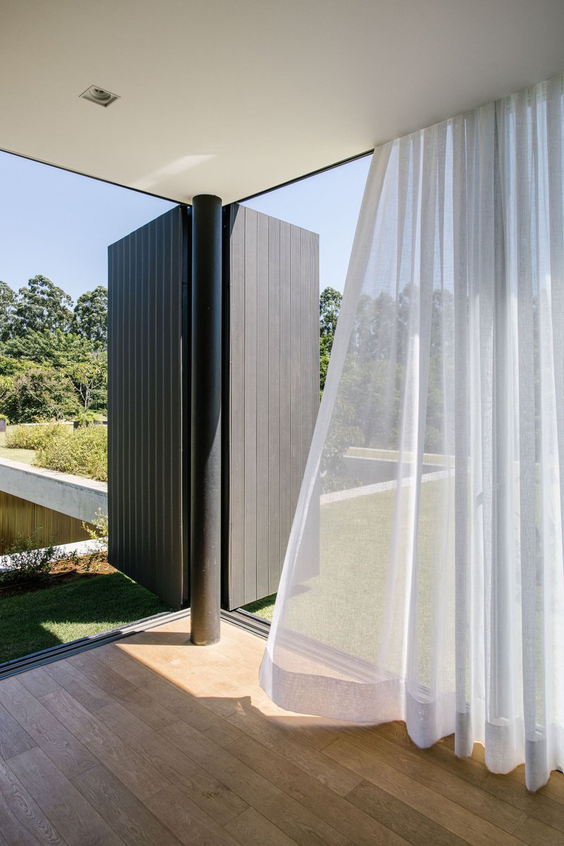Corner glazing with black pivot door and sheer curtain billowing in sunlight