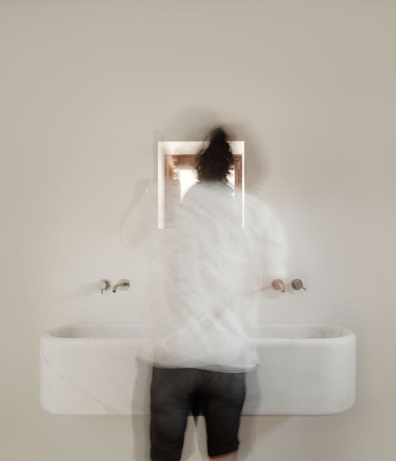 Blurred figure standing at a wall-mounted marble sink with recessed mirror niche above