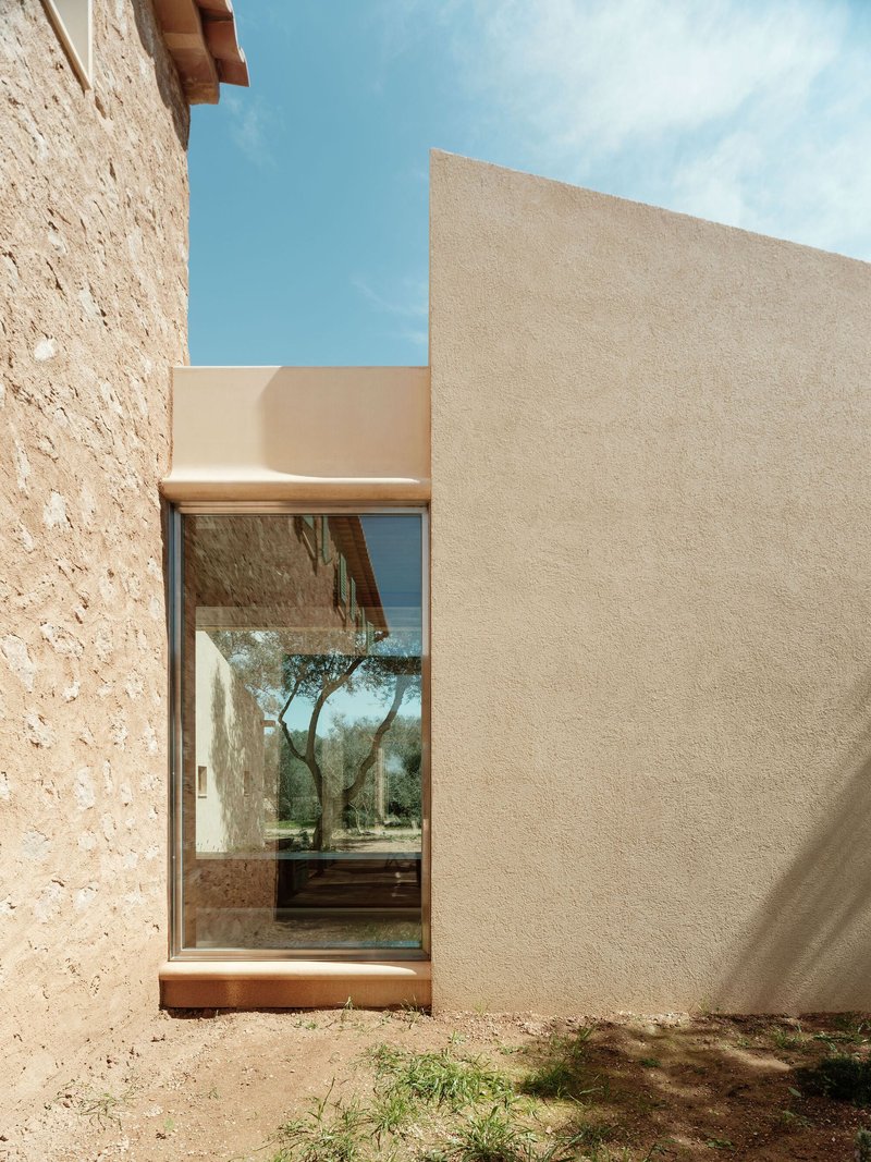 Glazed passage between stone and smooth plaster walls framing views of the olive grove beyond