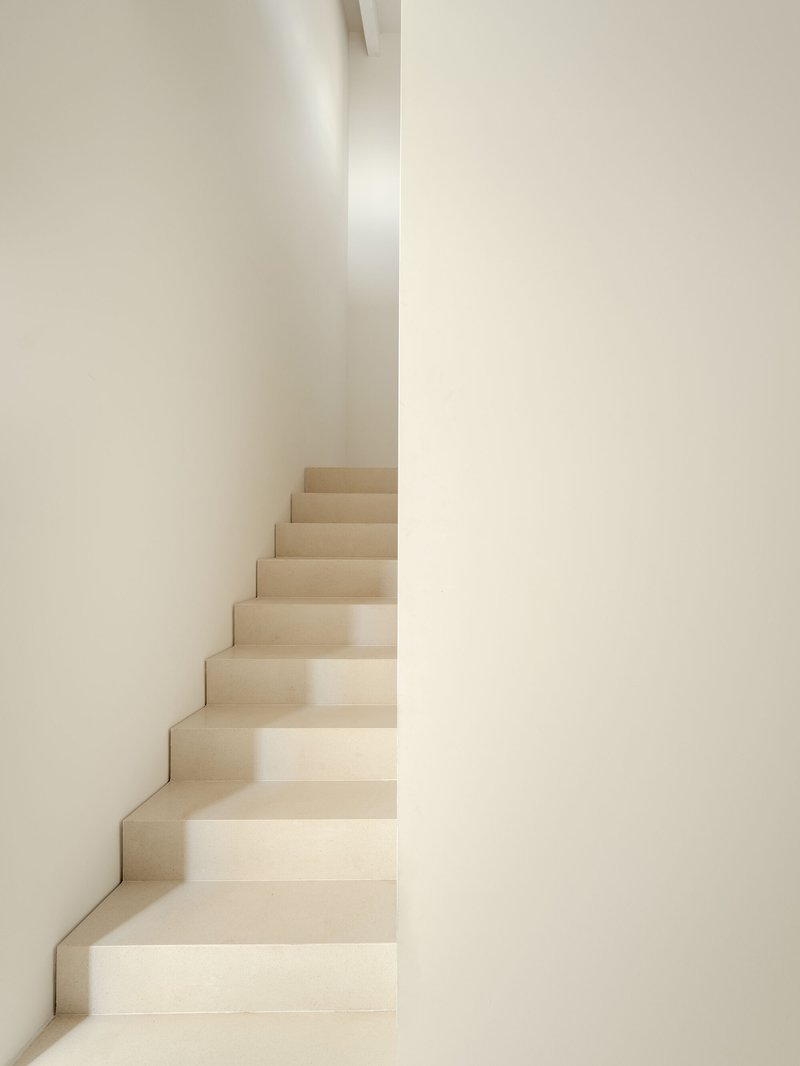 Narrow plastered staircase between converging white walls in soft natural light