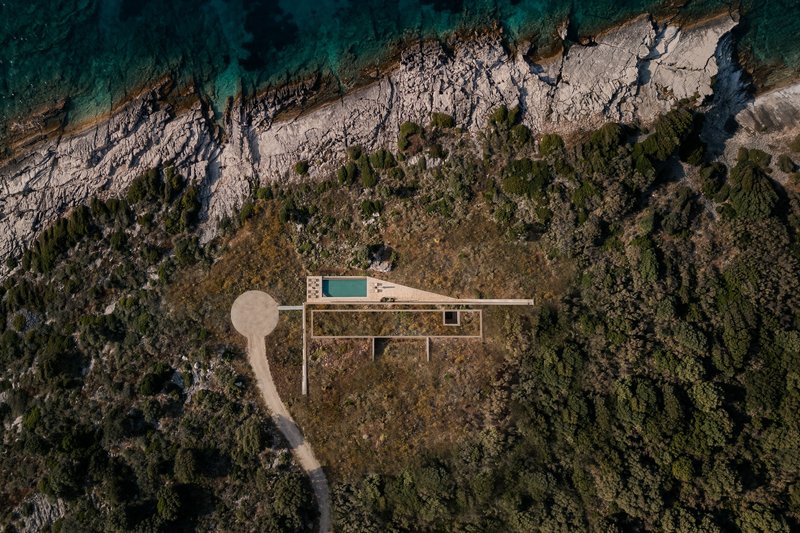 Aerial view of linear residence with swimming pool nestled between rocky coastal cliffs and dense Mediterranean vegetation