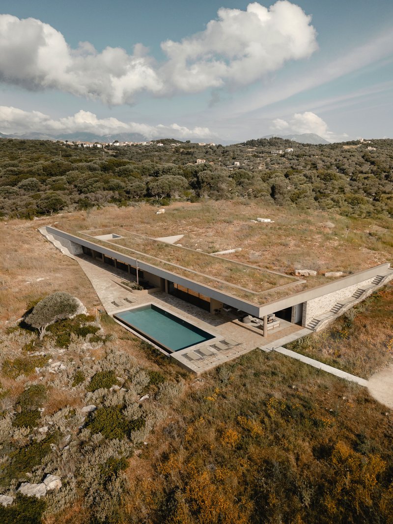 Drone view showing planted roof terrace and swimming pool terrace embedded in hillside with forested valley beyond