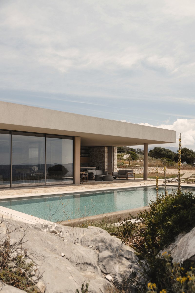 Covered terrace with stone wall and furniture overlooking rectangular pool edged by limestone outcrops and plantings